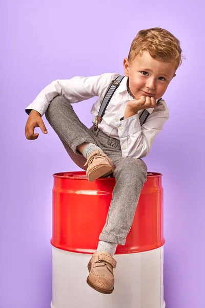 Adorable enfant garçon assis sur baril rouge en studio, posant à la caméra — Photo