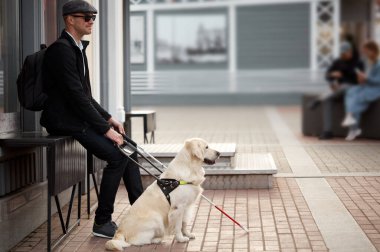 Engelli kişi dışarıda köpek rehberiyle oturup dinleniyor.