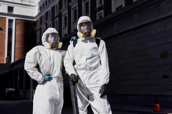 Desinfectantes profesionales en traje protector de materiales peligrosos caminando por las calles de la ciudad —  Fotos de Stock