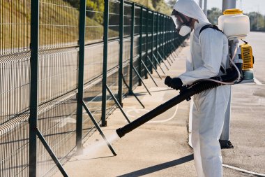 Tehlikeli giysideki genç dezenfektan mikroplu bölgede dezenfeksiyon yapıyor.