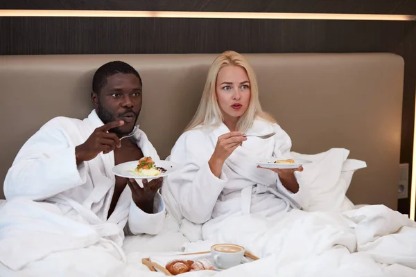 mixed race couple watch tv and have meal in hotel