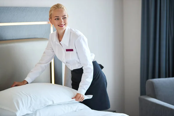 Bautiful maid setting up white pillow on bed sheet in hotel room — Stock Photo, Image