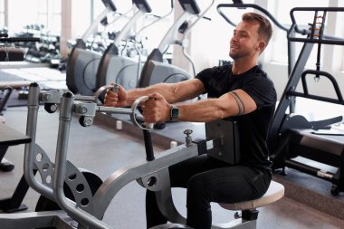 Kaslı adam spor salonunda makine üzerinde egzersiz yapar.