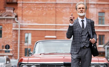 Gri saçlı ve sakallı zarif son sınıf öğrencisi dışarıda çantasıyla dolaşıyor.