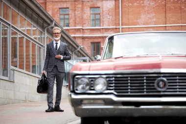 Gri saçlı ve sakallı zarif son sınıf öğrencisi dışarıda çantasıyla dolaşıyor.