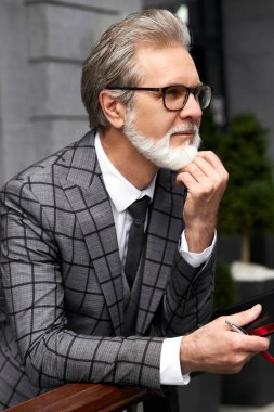 Ciddi 50-60 yıllık iş adamı dışarıda tefekkür içinde duruyor.