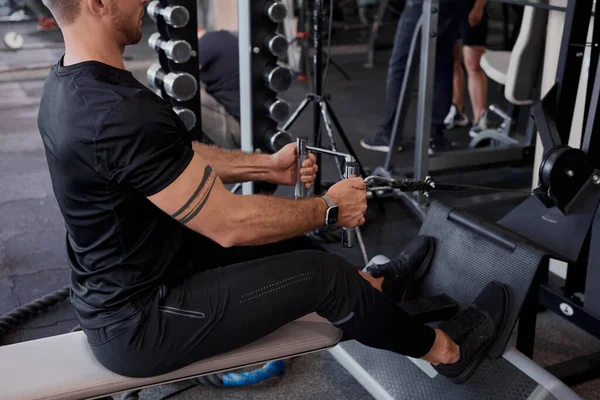 Kaslı adam spor salonunda makine üzerinde egzersiz yapar.