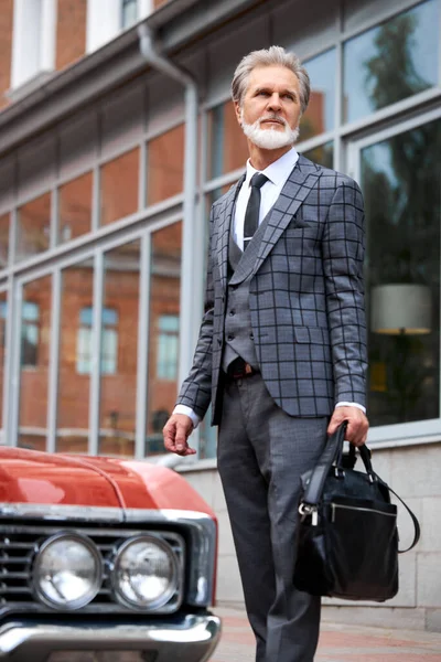Elegante hombre mayor con pelo gris y barba camina con bolsa al aire libre — Foto de Stock