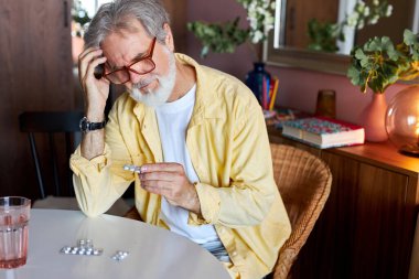 Yetişkin bir erkek elinde ilaç haplarıyla oturur.