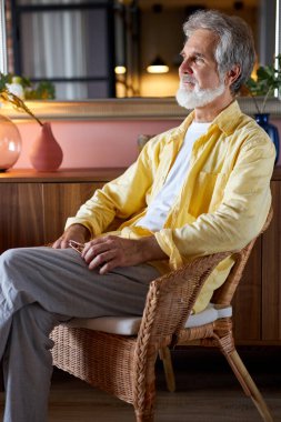 Sandalyede oturan yakışıklı, olgun bir adam başka tarafa bakıyor.