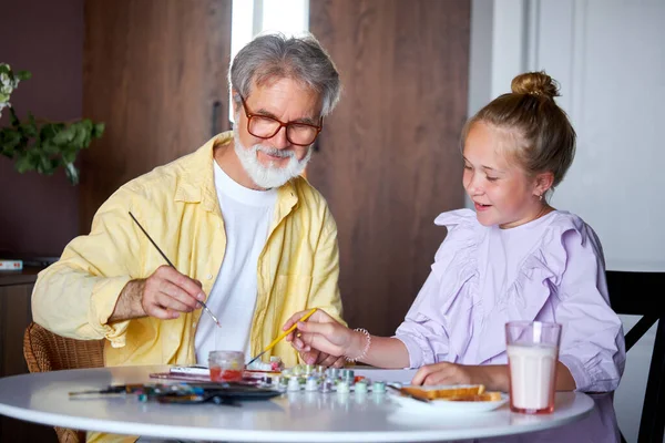 Bonito menina e sênior vovô pintura com tintas coloridas em casa — Fotografia de Stock