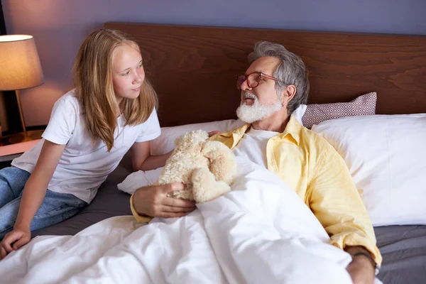 Menina entretém doente avô deitado na cama — Fotografia de Stock