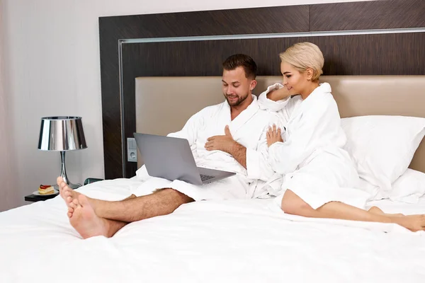 Beautiful couple lie on bed with laptop — Stock Photo, Image