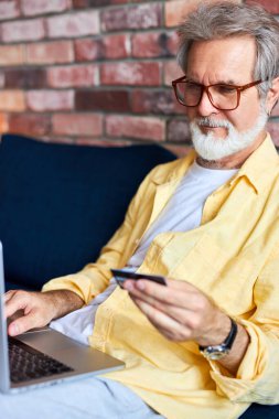 Evde kredi kartı ve dizüstü bilgisayarı olan olgun bir adam.