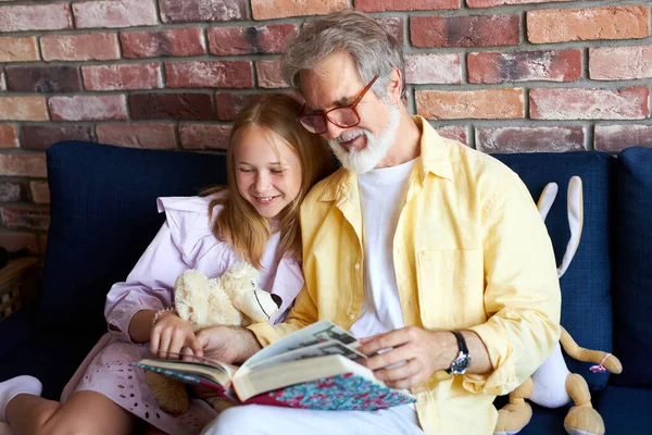 Senior man en klein meisje op zoek naar familie fotoalbum in de woonkamer — Stockfoto