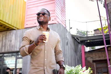 Afrikalı turist büyük şehirde yürüyüp kahve içiyor.