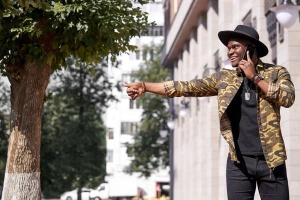 Hombre negro de piel oscura en ropa casual caminar y hablar por teléfono — Foto de Stock