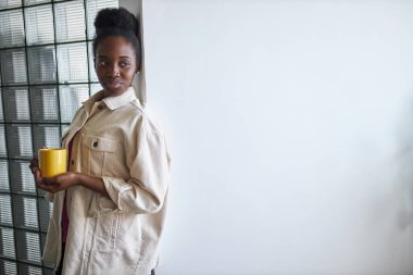 Gülümseyen siyah kadın kameraya bir fincan çay ya da kahve ile poz veriyor.