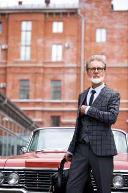 Gri saçlı ve sakallı zarif son sınıf öğrencisi dışarıda çantasıyla dolaşıyor.