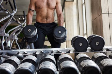 Gömleksiz genç adam pazılar için ağır ağırlık egzersizi yapıyor.