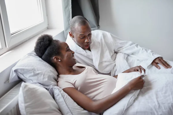 Black afroamerican man suprisingly looks at pregnant wifes belly — Stock Photo, Image