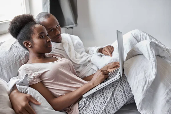 Όμορφο ευτυχισμένο ζευγάρι που χρησιμοποιεί φορητό υπολογιστή στο κρεβάτι — Φωτογραφία Αρχείου