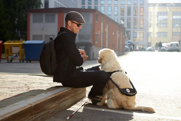 Side view on handsome guy sitting outdoors, playing with dog — Stock Photo, Image