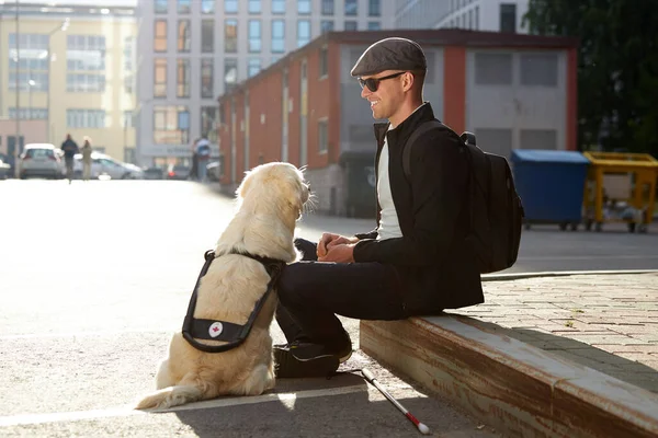 Side view on handsome guy sitting outdoors, playing with dog — Stock Photo, Image