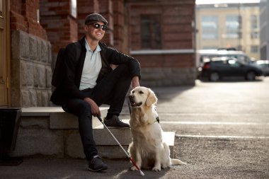 Engelli kişi dışarıda köpek rehberiyle oturup dinleniyor.