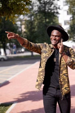 Esmer tenli siyah adam, günlük kıyafetlerini giyiyor, yürüyor ve telefonda konuşuyor.