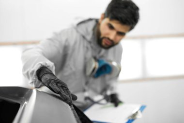 Üniformalı beyaz tenli yakışıklı tamirci otomobil servisinde arabaları incelerken notlar alıyor.