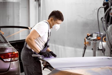 Beyaz tenli tamirci, araba zımparalıyor ve araba boyamaya hazırlanıyor.