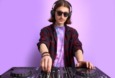Güneş gözlüklü beyaz stil DJ 'i mor stüdyo arka planında konsolu karıştırıyor.