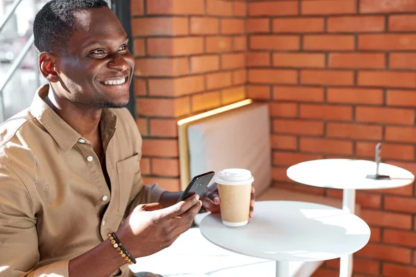 Hombre africano joven con teléfono inteligente en la cafetería —  Fotos de Stock