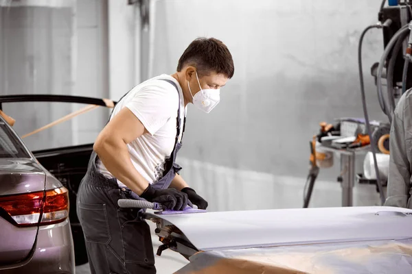 Beyaz tenli tamirci, araba zımparalıyor ve araba boyamaya hazırlanıyor.