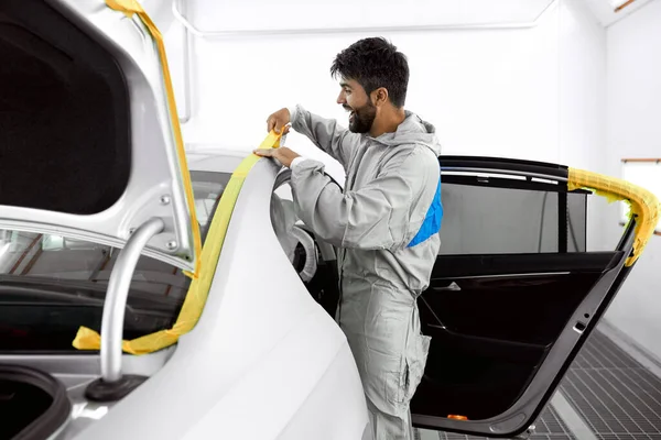 young car mechanic applying masking tape to a sanded down car before a paint job