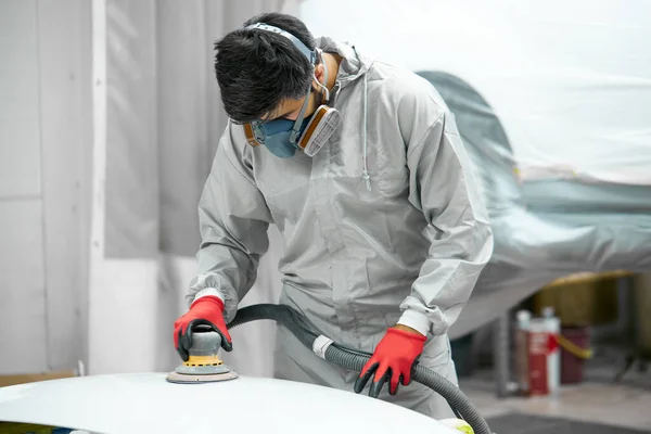 Jovem limpador de carro caucasiano no respirador e óculos de proteção carro de polimento com máquina — Fotografia de Stock