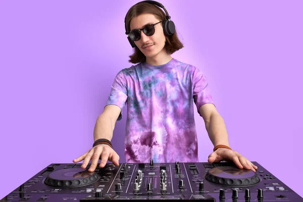 紫色工作室背景下戴太阳镜混音控制台的卡卡式时尚DJ. — 图库照片