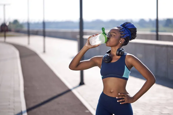 black gorgeous woman fitness instructor drinking water during the training exercises outdoors
