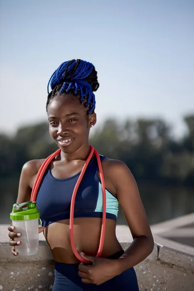 ウォーターボトルとスキップロープを持つ幸せなスポーツアフリカの女性の肖像画 — ストック写真