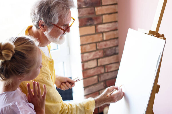 portrait of senior man, grandfather teaching girl painting