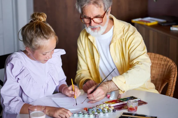 cute little girl and senior granddad painting with colorful paints at home