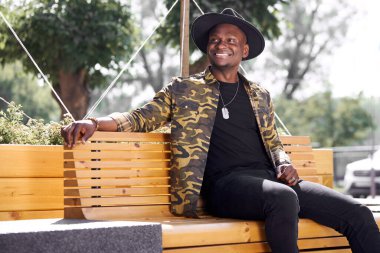 Gülümseyen siyah adam tek başına bankta oturuyor.