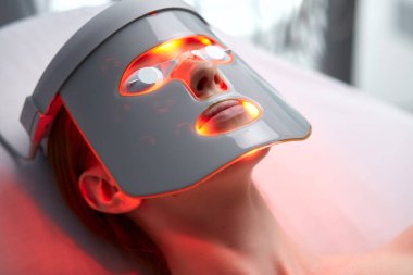woman in LED mask, getting skin rejuvenation therapy in aesthetic clinic clipart