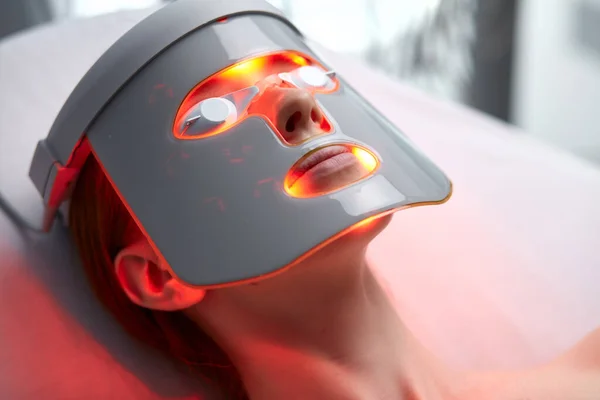 woman in LED mask, getting skin rejuvenation therapy in aesthetic clinic