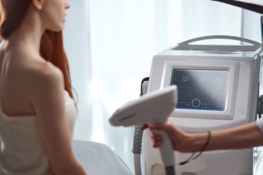 Masaj masasındaki kızıl saçlı kadın kozmetik uzmanı tarafından elektrik masajı yaptırıyor.