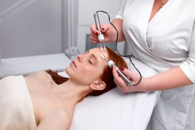 Profesyonel kozmetik uzmanı güzellik prosedürü uygularken özel bir cihaz tutuyor.