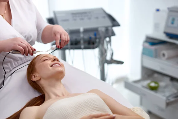 Cosmetólogo profesional sosteniendo un dispositivo especial mientras realiza un procedimiento de belleza —  Fotos de Stock