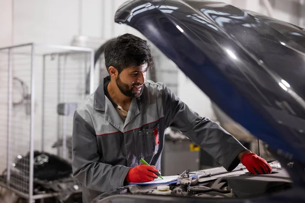 Bebaarde auto monteur motor prestaties in de motorkap van de auto — Stockfoto