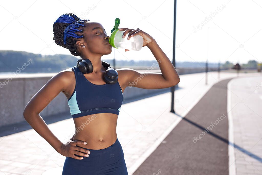 black gorgeous woman fitness instructor drinking water during the training exercises outdoors